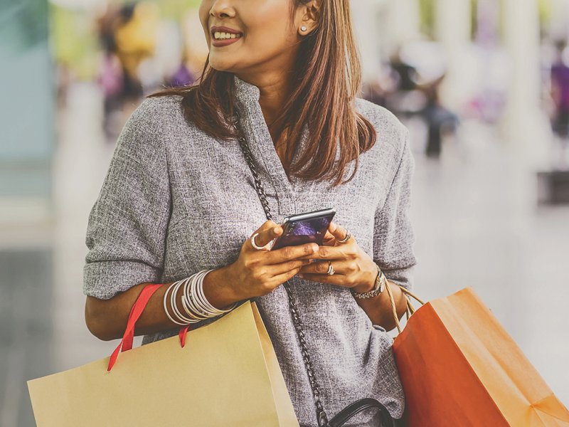 woman with shopping bags who is holding a phone with both hands and smiling